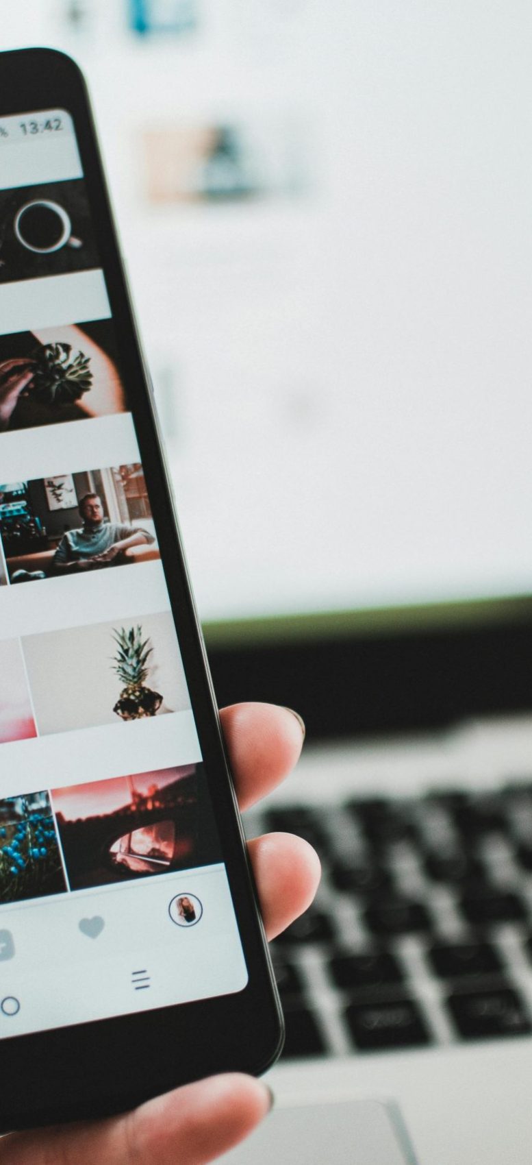 A person uses a smartphone to browse social media in front of a laptop, emphasizing modern technology and lifestyle.